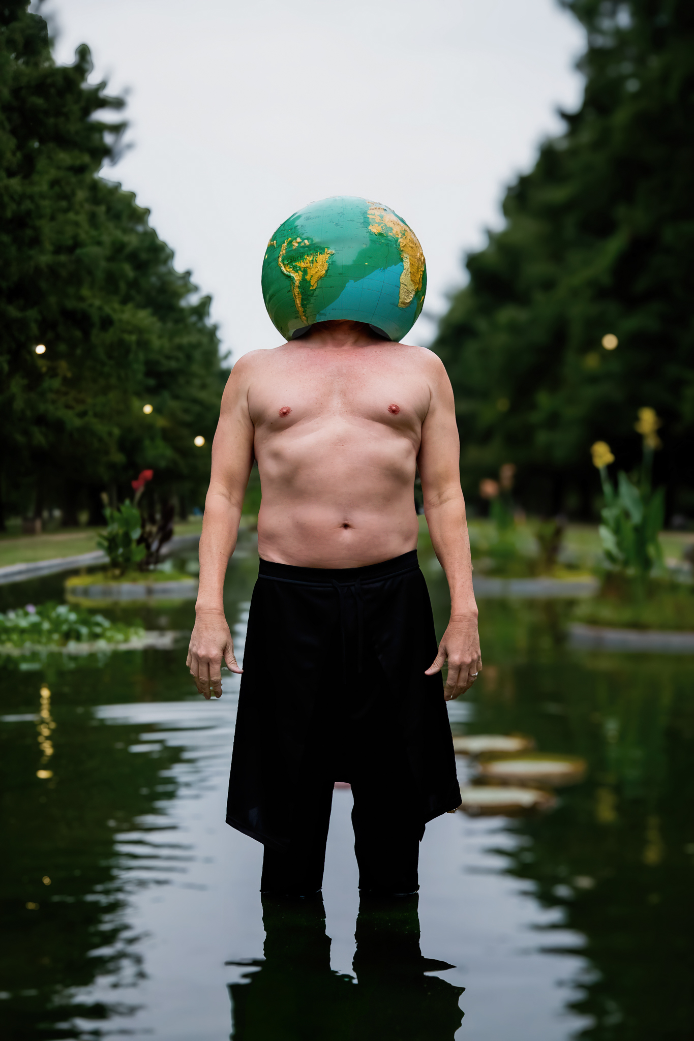 Portrait wearing an inflatable globe over the head, standing in a reflecting pool